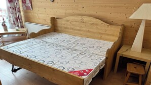 A wooden bed with a patterned mattress, a bedside table, a lamp, and a small stool. - Les 2 alpes, at the foot of the slopes - apartments (Les Deux Alpes)
