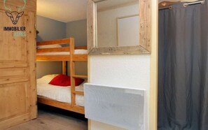 Un lit superposé avec un oreiller rouge, une armoire en bois, un miroir et un rideau de douche.