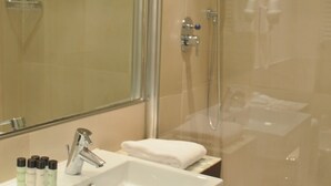 Un baño con cabina de ducha de vidrio, un lavabo blanco y un espejo.