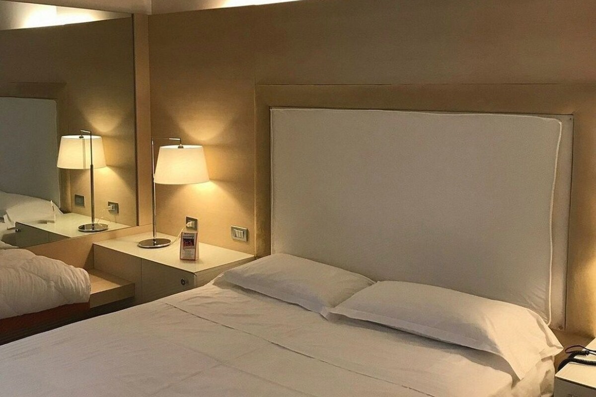 A hotel room with a large bed, two bedside lamps, a nightstand, and a mirror.