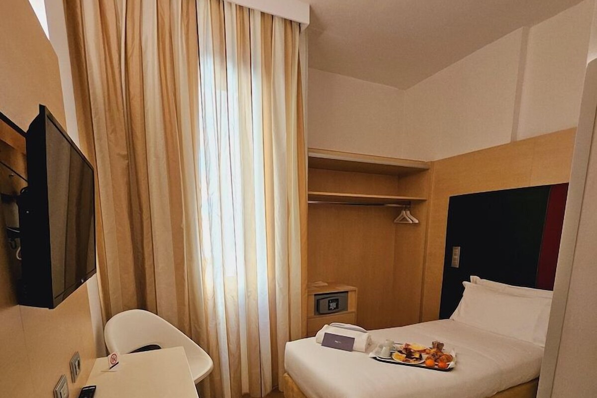 Une chambre d’hôtel comprenant un lit, un bureau, une chaise, une télévision et une armoire.