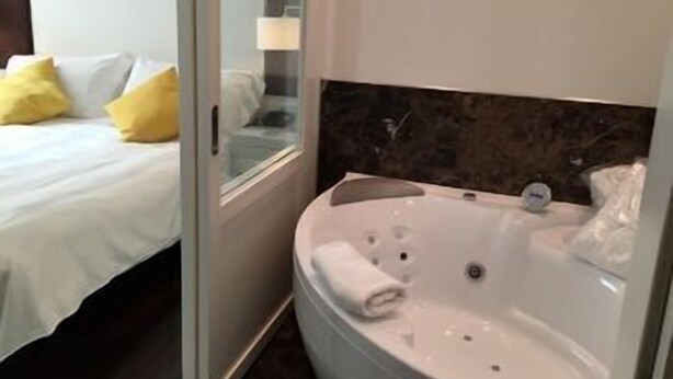 Habitación de hotel con cama, cabina de ducha de vidrio y bañera.