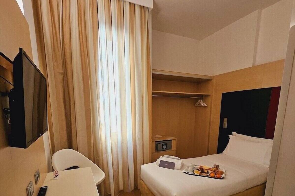 Una habitación de hotel con una cama, un escritorio, una silla, un televisor y un armario.