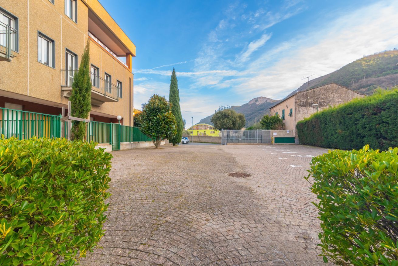 A courtyard with a paved ground, a building with balconies, and a mountain in the background.
