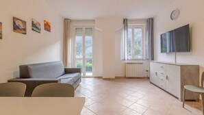 Una sala de estar con sofá, sillas, televisor, radiador y ventana con cortinas.
