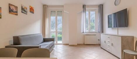A living room with a sofa, chairs, a TV, a radiator, and a window with curtains.