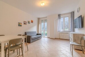 A spacious room with a dining table, a sofa, a TV mounted on the wall, and a window with curtains.