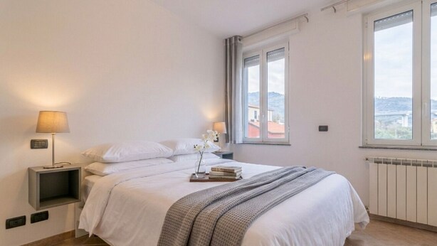 Un dormitorio con cama, mesitas de noche, lámparas, una ventana con vistas y un radiador.