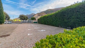 Un estacionamiento pavimentado con un seto verde y un edificio al fondo.