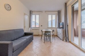 Una sala de estar con un sofá, una mesa de comedor con sillas, un televisor y una ventana con cortinas.