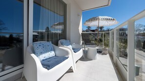 Ein Balkon mit zwei weißen Stühlen, einem kleinen Tisch und einem gestreiften Sonnenschirm.