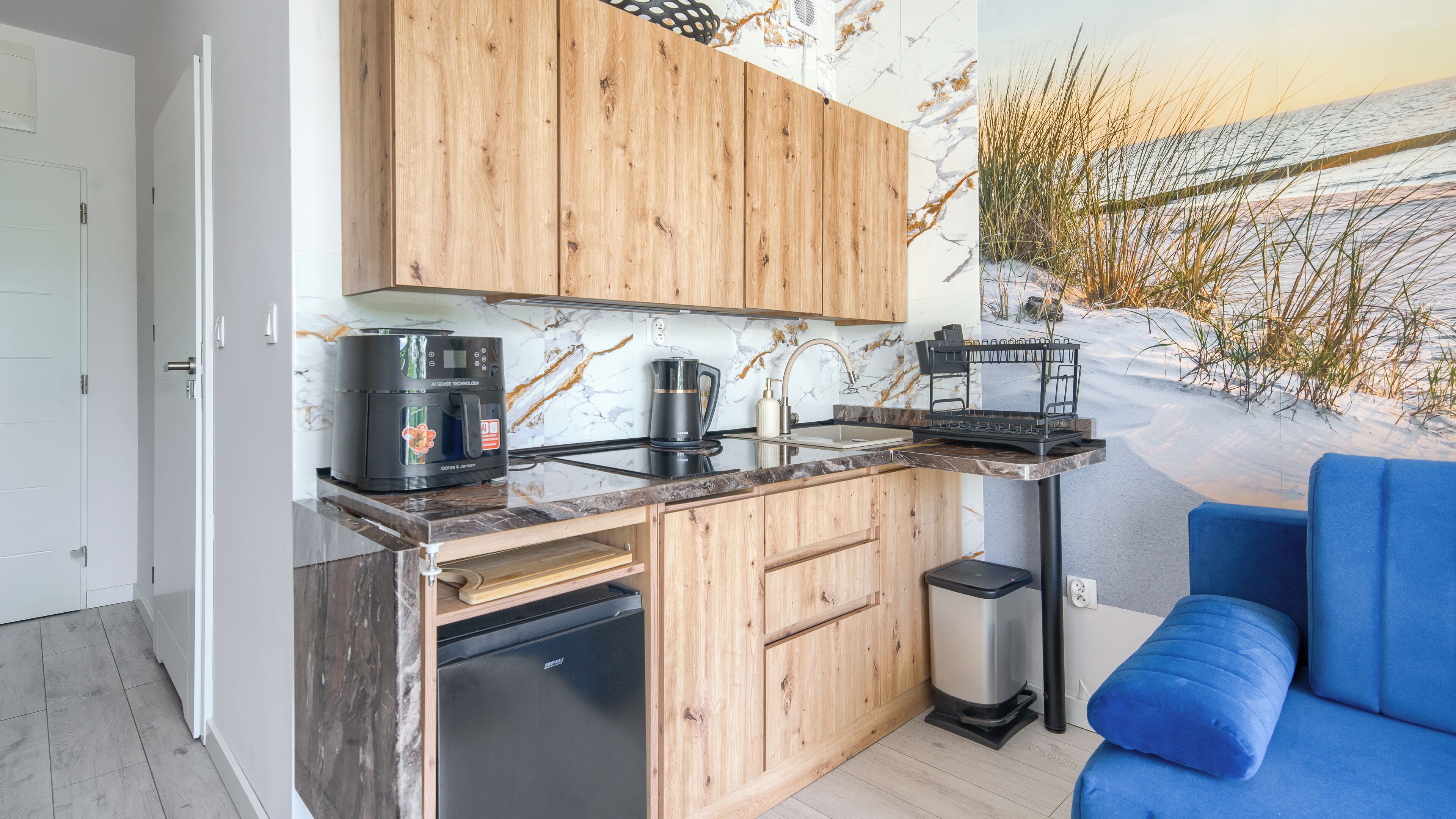 Una cocina moderna con armarios de madera, cafetera, hervidor y un cubo de basura.