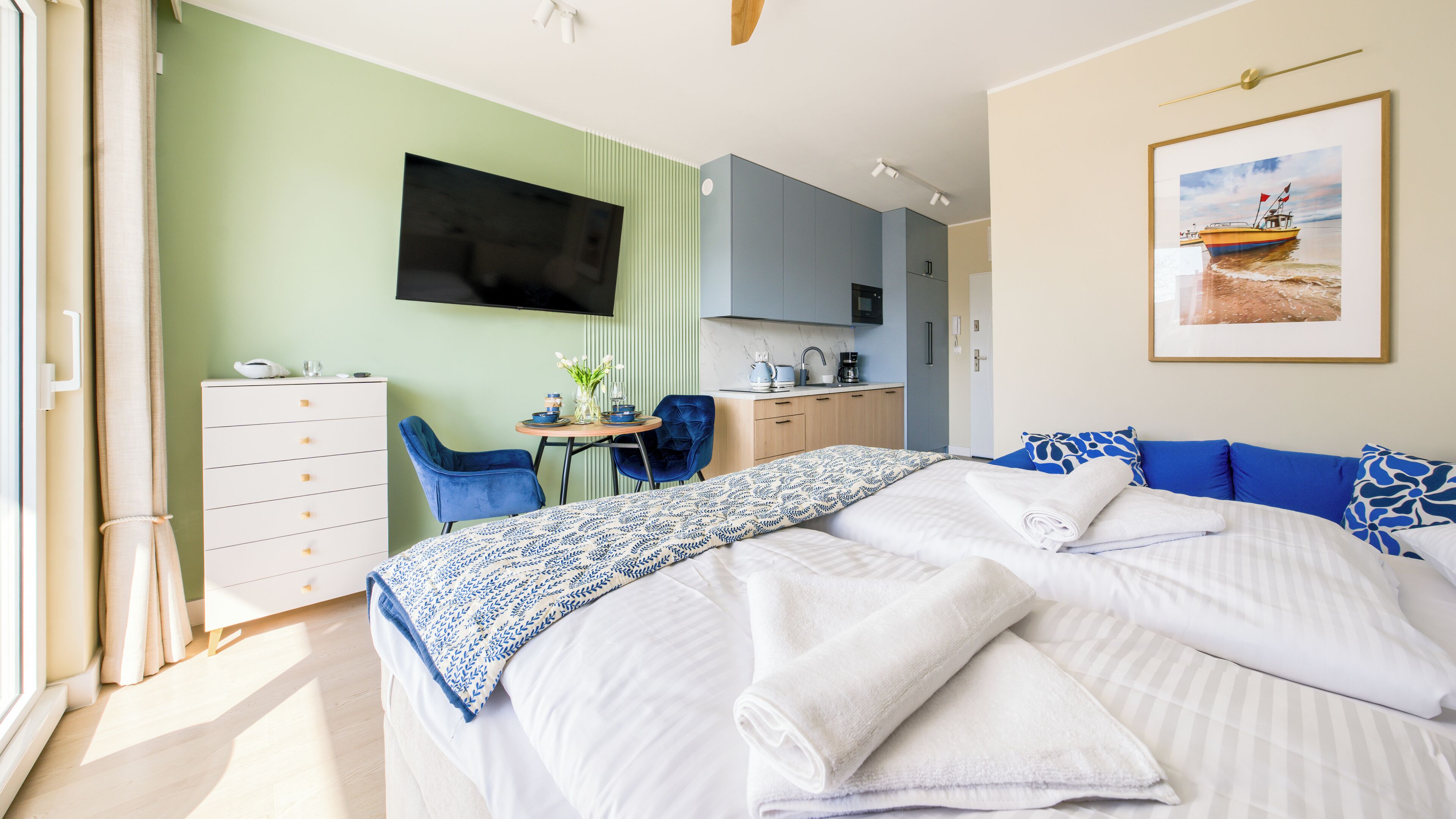 Ein Schlafzimmer mit Bett, Schreibtisch, Stuhl, Fernseher und Küchenzeile.