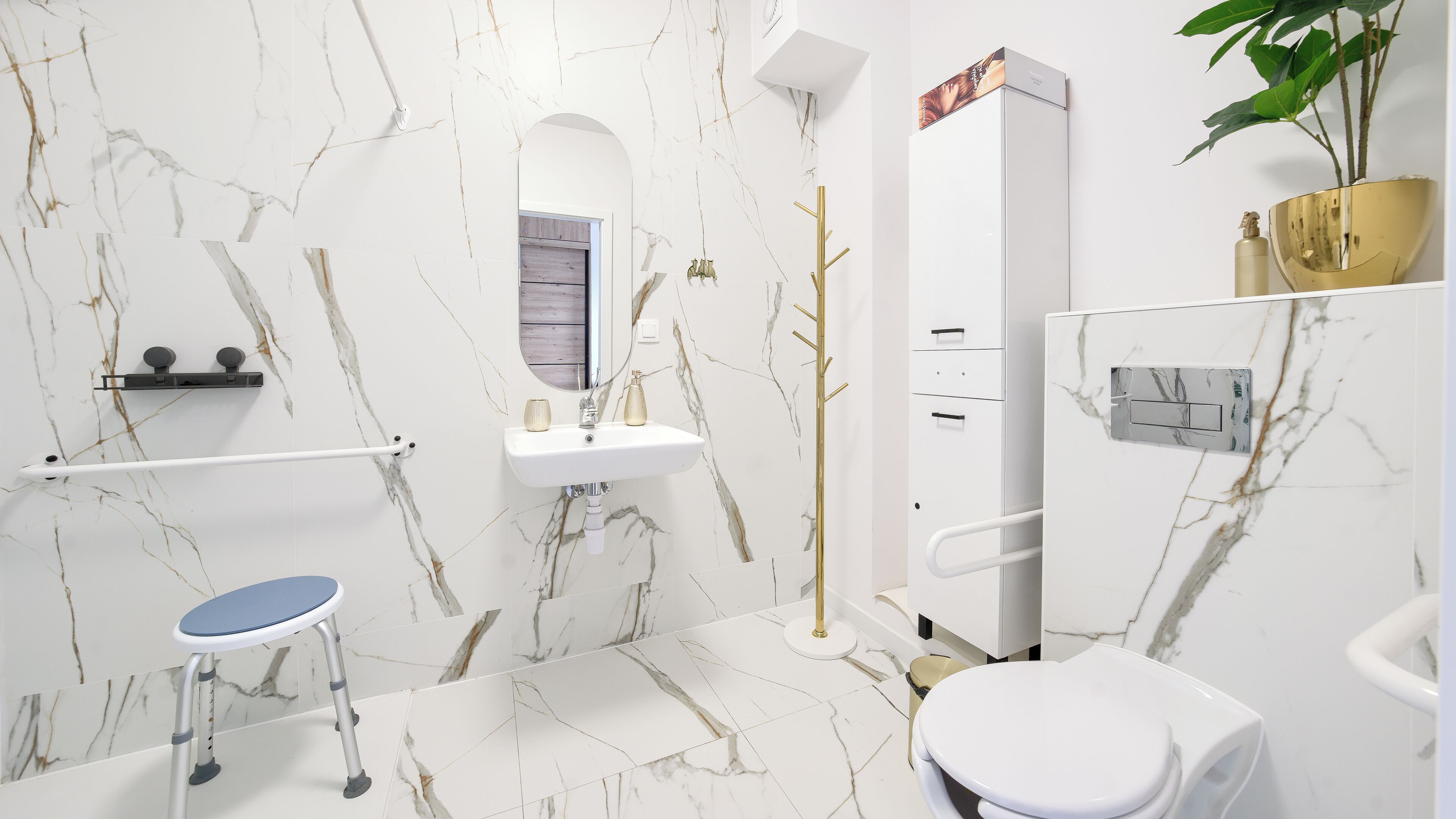 Ein Badezimmer mit Marmorwand, Waschbecken, Toilette, Ablagefläche und einer Pflanze.