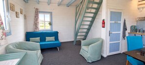 A room with a blue sofa, two green armchairs, a ladder, a door with a blue panel, and a small table with a chair.