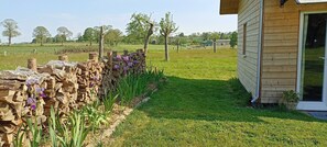 A stone wall with a wooden structure adjacent to a grassy field and trees in the background.