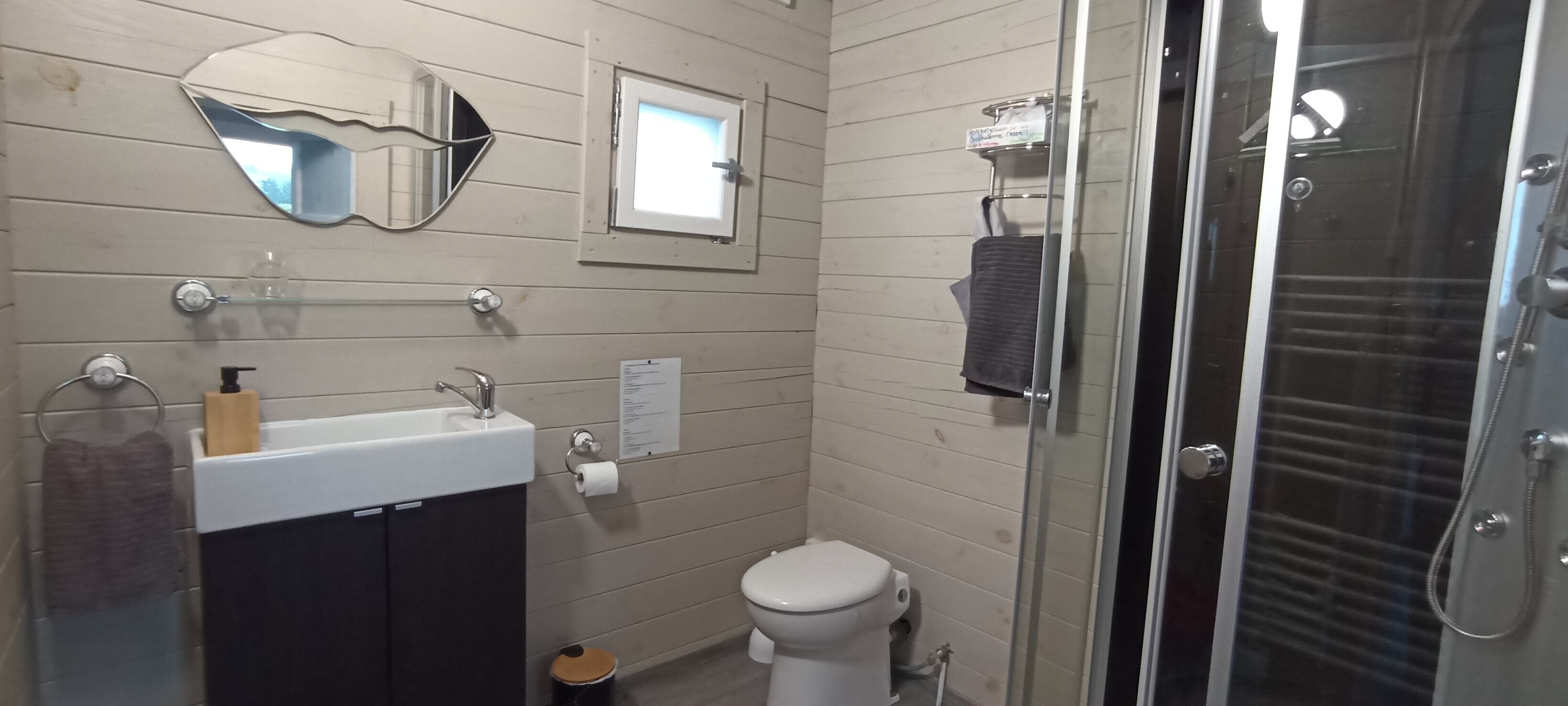 Un baño con lavamanos, espejo, inodoro y cabina de ducha con mampara de vidrio.
