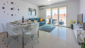 A modern living space with a dining area, a sofa, a coffee table, and a TV. - Modern apartment with sun terrace and sea view (Crikvenica)