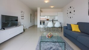 A modern living room with a flat-screen TV, a glass coffee table with flowers, a sofa with a yellow pillow, and a kitchen in the background. - Modern apartment with sun terrace and sea view (Crikvenica)