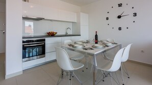 A modern kitchen with white cabinets, a stainless steel oven, and a dining area with a glass table and white chairs. - Modern apartment with sun terrace and sea view (Crikvenica)