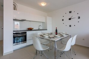 A modern kitchen with white cabinets, a stainless steel oven, and a dining area with a glass table and white chairs. - Modern apartment with sun terrace and sea view (Crikvenica)