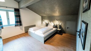 Un dormitorio con cama, mesitas de noche, una ventana con cortinas, un radiador y una puerta.