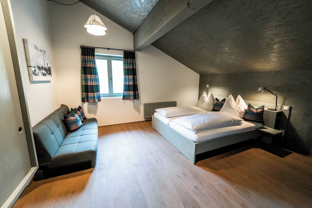 A bedroom with a bed, a sofa, a window with curtains, a radiator, and a lamp.