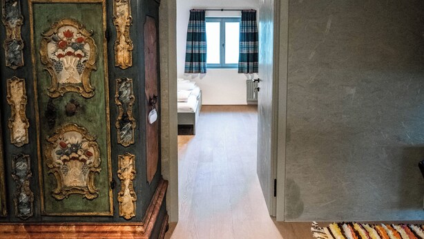 Un pasillo que conduce a un dormitorio con una cama, un tocador y una alfombra estampada.