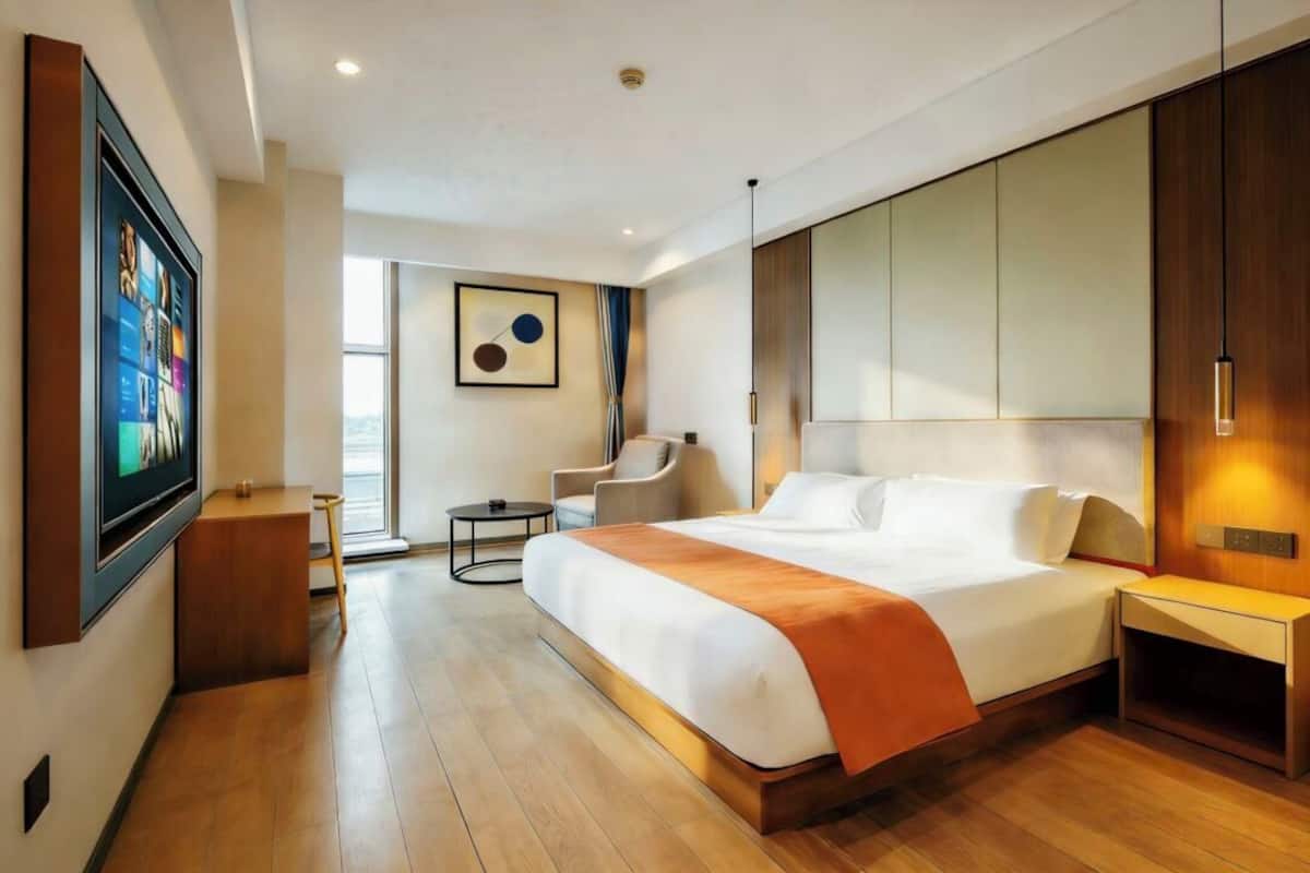 A modern hotel room with a large bed, a desk, a chair, and a TV mounted on the wall.