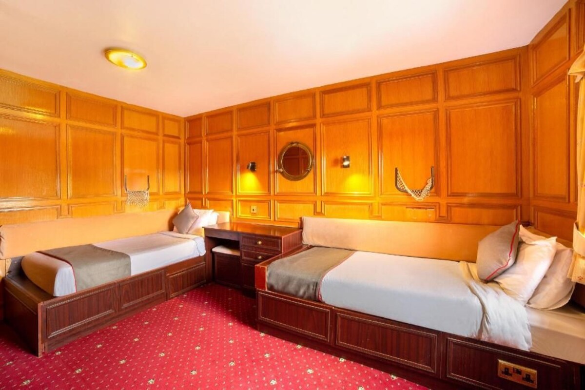 Een hotelkamer met twee eenpersoonsbedden, een wand van houten panelen, een rood geweven tapijt en een ronde spiegel boven het hoofdeinde.