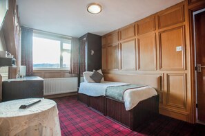 Una habitación con cama, una mesa, un radiador y una ventana con cortinas.