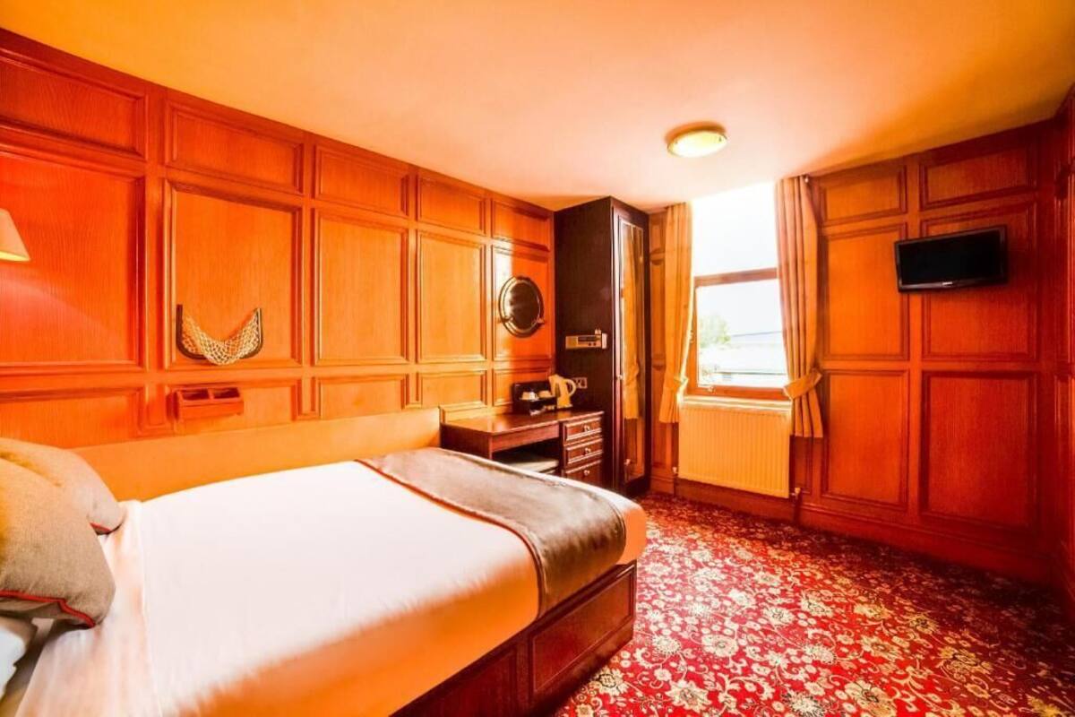 Una habitación de hotel con cama, paneles de madera, televisor, escritorio y ventana.