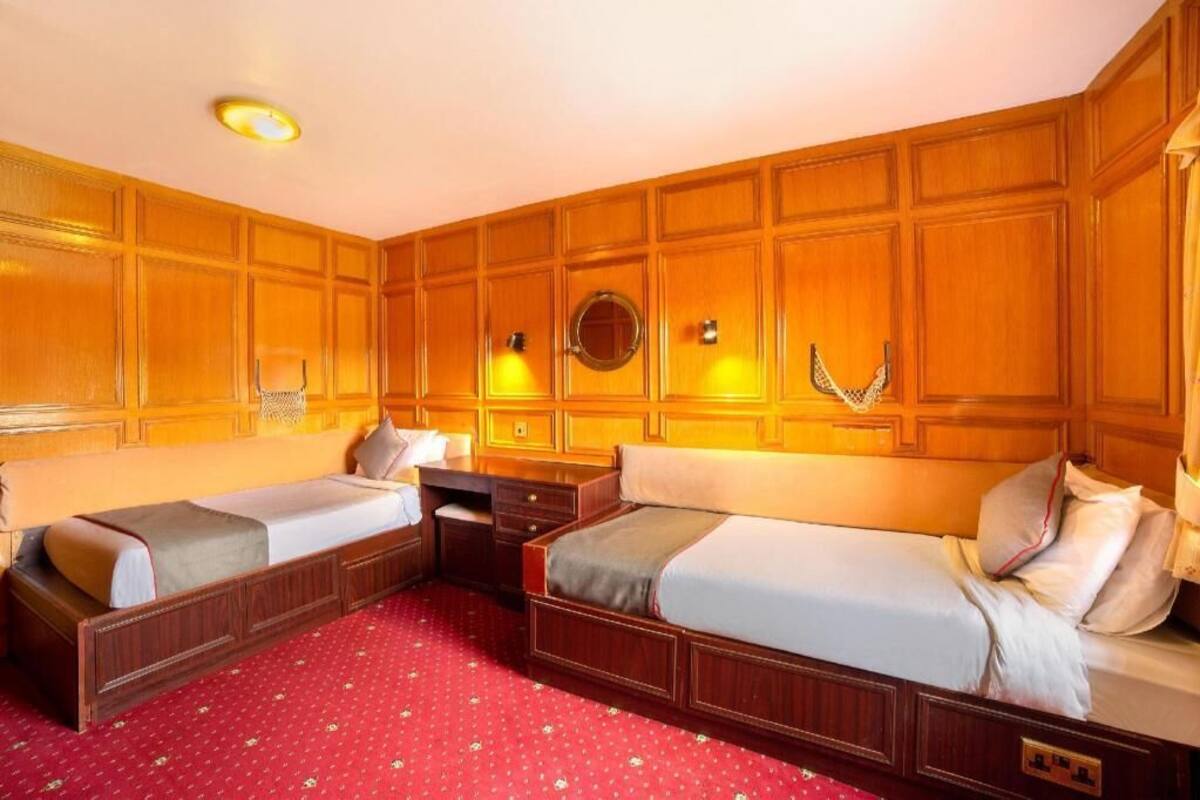Habitación de hotel con dos camas individuales, un cabecero de panel de madera, una alfombra roja estampada y un espejo redondo sobre el cabecero.