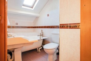 Un baño con una bañera independiente, inodoro y tragaluz.