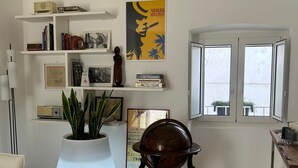 Een kamer met een witte bank, een wereldbol op een standaard, een kamerplant, een boekenplank en een raam met uitzicht.