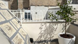 Een balkon met een bloempot, een witte reling en een stenen gebouw op de achtergrond.