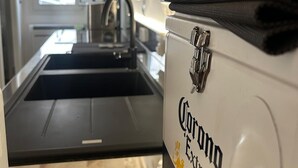 Een keuken met een roestvrijstalen spoelbak, een kraan en een aanrecht. Op het aanrecht staat een fles Corona Extra bier en een zwarte spatel.