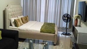 A hotel room with a bed, a sofa, a glass coffee table, a fan, and a TV. - Relax in Style: Fully Furnished Studio Apartment. Secure and amazing in Nairobi (Nairobi)