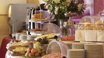 A buffet with various food items, including fruits, meats, and pastries, arranged on a table with a clear glass dome covering some dishes.