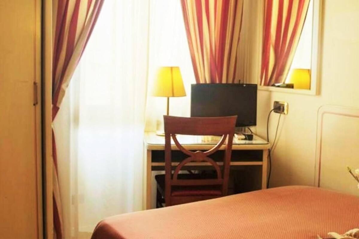 A hotel room with a bed, a desk with a computer, a chair, and curtains.