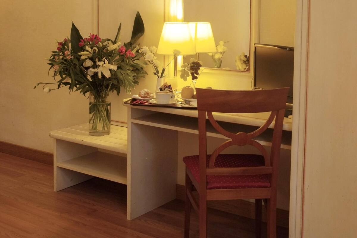 A wooden desk with a lamp, a chair, and a vase of flowers.