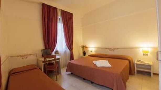 A hotel room with two beds, a desk, a chair, a nightstand, and a lamp. - Hotel Villa Rosa (Modica)