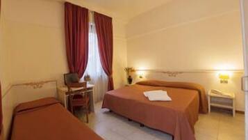 A hotel room with two beds, a desk, a chair, a nightstand, and a lamp.