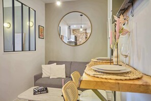 Een eethoek met een houten tafel, stoelen, een spiegel en uitzicht op een zithoek met een bank en een bakstenen muur.