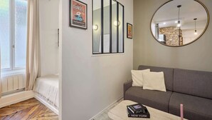 Un soggiorno moderno con un divano grigio, un piccolo tavolino da caffè con libri, uno specchio e un quadro incorniciato appeso al muro.