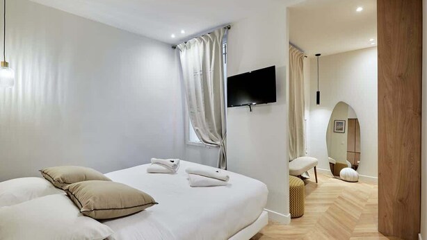 Une chambre d’hôtel moderne avec un grand lit, un téléviseur à écran plat fixé au mur et un plancher en bois.