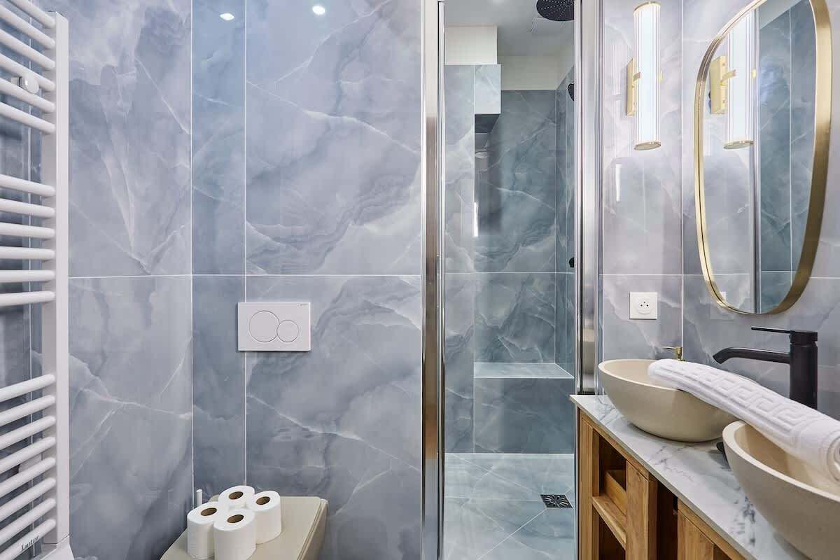 A modern bathroom with marble walls, a glass shower enclosure, and a vanity with two sinks.
