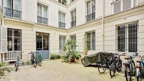 Une cour avec un sol carrelé, des plantes en pot et des vélos garés le long des murs.