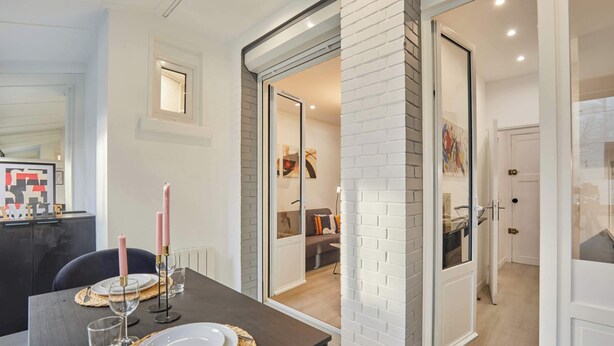 A dining area with a table set for two, a kitchen visible through an open door, and a living area in the background. - Modern Suite with Patio Boulogne-Billancourt (Boulogne-Billancourt)