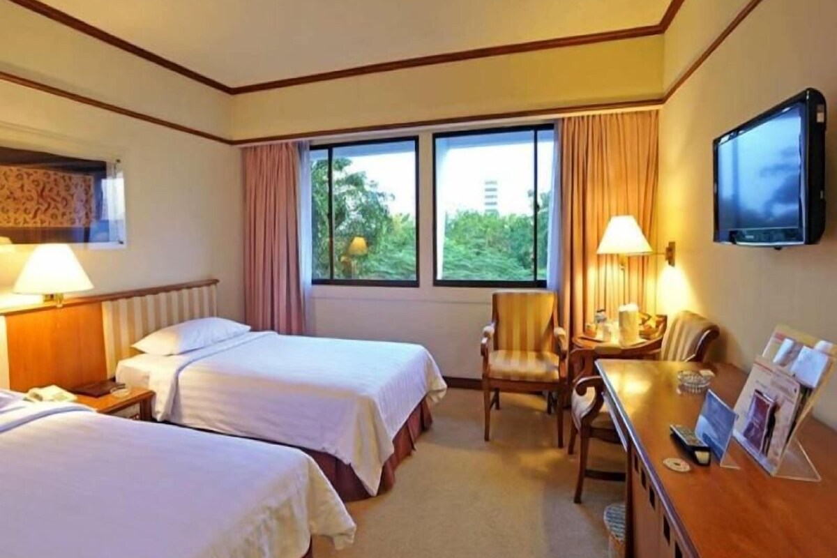 A hotel room with two beds, a desk with a chair, a television, and a window with curtains.